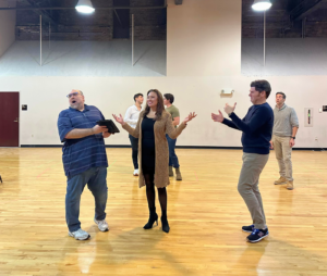 An actress, center, responds to two actors on either side of her as the chorus performs in the background