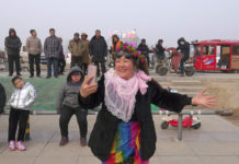 a smiling woman dressed in festive garb films herself and the crowd behind her with her mobile phone