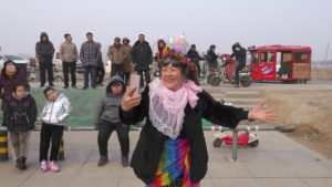 a smiling woman dressed in festive garb films herself and the crowd behind her with her mobile phone
