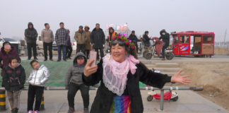 a smiling woman dressed in festive garb films herself and the crowd behind her with her mobile phone
