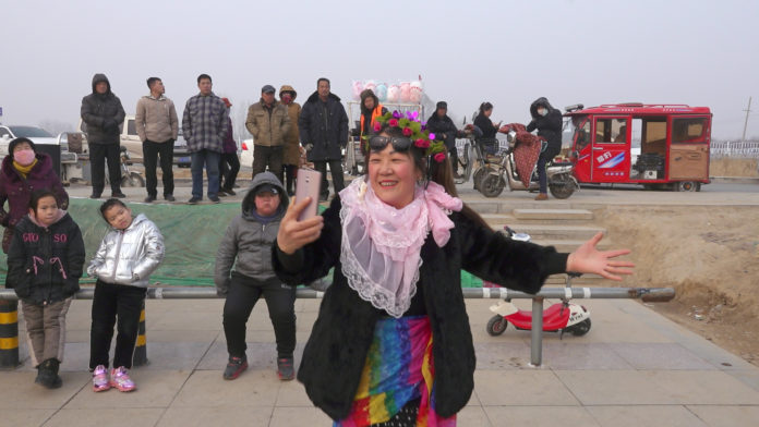 a smiling woman dressed in festive garb films herself and the crowd behind her with her mobile phone