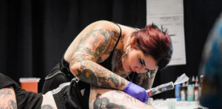 a woman tattoos another woman's thigh as she rests on a table