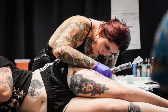 a woman tattoos another woman's thigh as she rests on a table