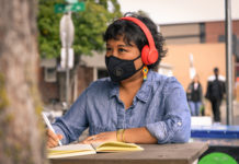 a woman wearing headphones and a mask over her nose and mouth writes in a notebook