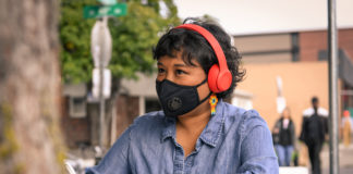 a woman wearing headphones and a mask over her nose and mouth writes in a notebook