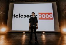 musician stands in front of a large screen displaying the name of his music project