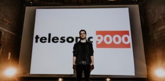 musician stands in front of a large screen displaying the name of his music project
