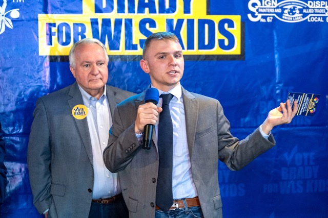 Brady Hall w Sarantou young man wearing a jacket and tie holds a microphone