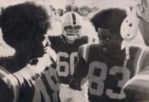 two football players huddle to talk, surrounded by teammates