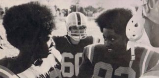 two football players huddle to talk, surrounded by teammates