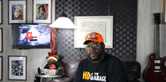 A man in a room with pictures and a guitar hanging in the background.