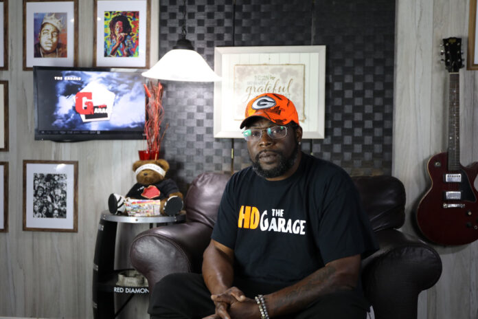 A man in a room with pictures and a guitar hanging in the background.