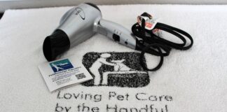 A white towel with the company's name and logo under a silver blow dryer and business card.
