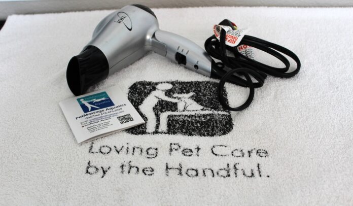 A white towel with the company's name and logo under a silver blow dryer and business card.