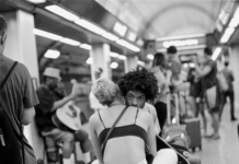 Art to Heart: James “dirtykics” Dickerson A man sitting on a bench in a crowded public place leaning against a woman who is nestled against him as well.