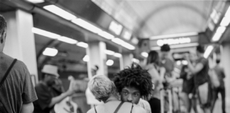 A man sitting on a bench in a crowded public place leaning against a woman who is nestled against him as well.