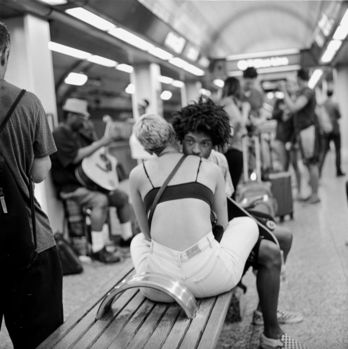A man sitting on a bench in a crowded public place leaning against a woman who is nestled against him as well.