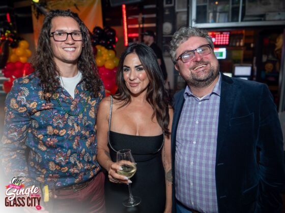 Left a man with long curly hair, in the center is a woman in a black dress and on the right is a man with shorter hair in a suit.