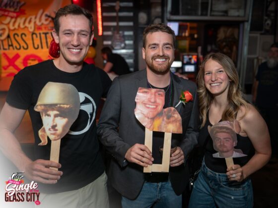 (left and center) two men holding a head cut out. On the right is a woman holding a head cut out as well.