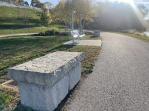 Cement bolders stacked together as benches facing the Maumee River, as well as a metal swinging bench in the background.